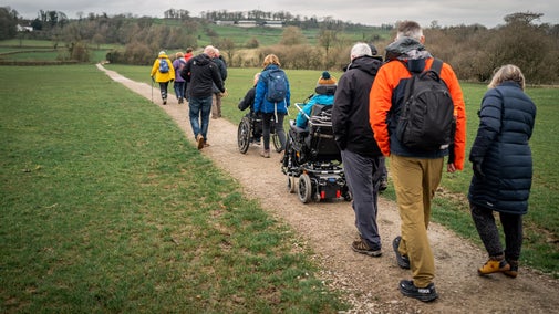 Group of people, including two people on powered mobility vehicles, walking through the field on the Holeslack accessible route